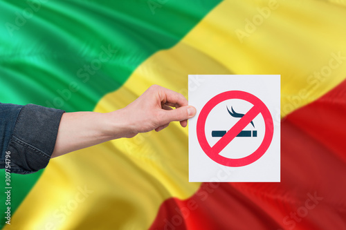Republic Of The Congo health concept. Hand holding paper with no smoking sign over national waving flag. Quit smoke theme.