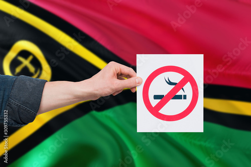 Vanuatu health concept. Hand holding paper with no smoking sign over national waving flag. Quit smoke theme.