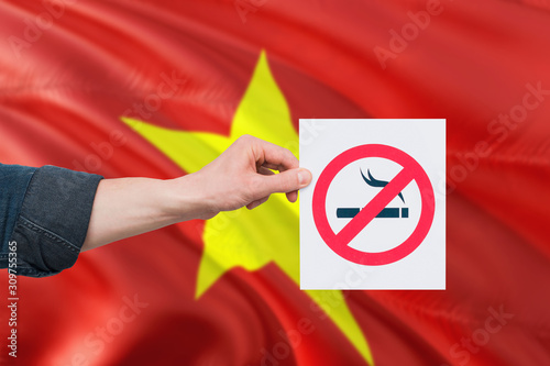 Vietnam health concept. Hand holding paper with no smoking sign over national waving flag. Quit smoke theme.
