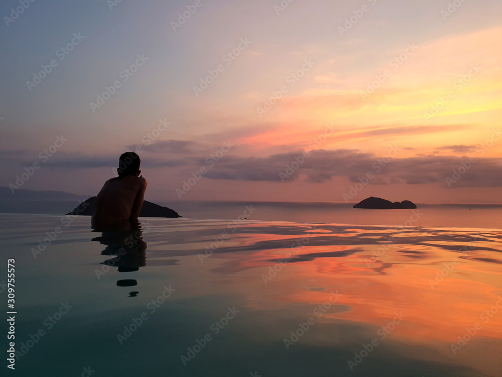 Scenic sunset from infinity pool with orange to purple gradient reflections on water surface on Koh Phangan island, Thailand