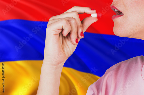 Armenia health care concept. Close-up of a woman taking vitamin capsule on national flag background.