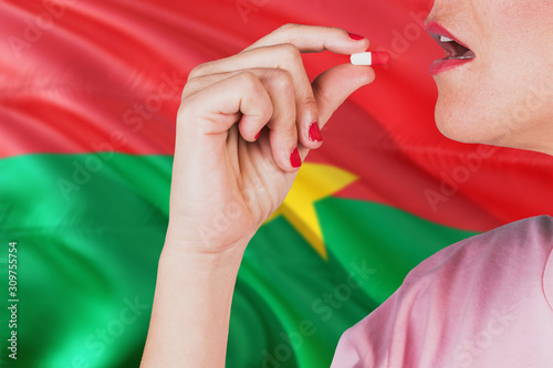 Burkina Faso health care concept. Close-up of a woman taking vitamin capsule on national flag background.