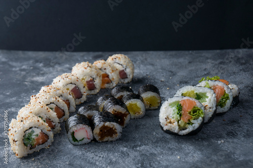 Different sushi on a dark textured background, fresh futomaki, uramaki and hosomaki.