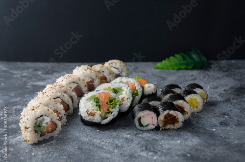 Different sushi on a dark textured background, fresh futomaki, uramaki and hosomaki.