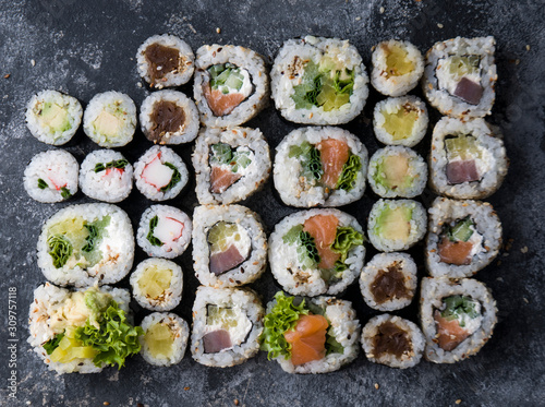 Different sushi on a dark textured background, fresh futomaki, uramaki and hosomaki.