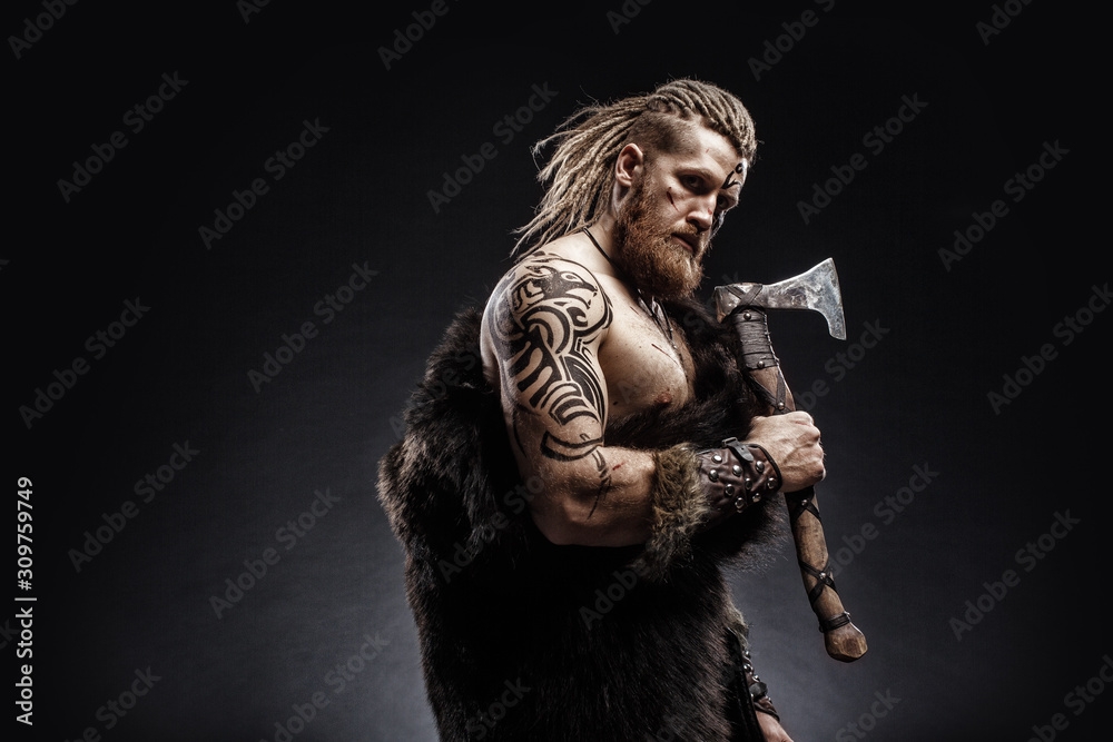 Medieval warrior berserk Viking with tattoo with axes attacks enemy. Concept historical photo Medieval warrior berserk Viking with tattoo with axes attacks enemy. Concept historical photo
