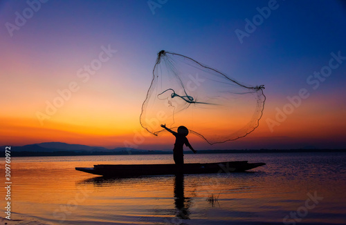 Asia fisherman net using on wooden boat casting net sunset or sunrise in the Mekong river - Silhouette fisherman boat with mountain background life person countryside