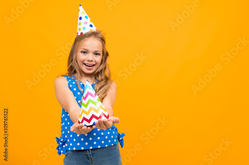 happy girl holds out a festive cap on an orange background with copy space