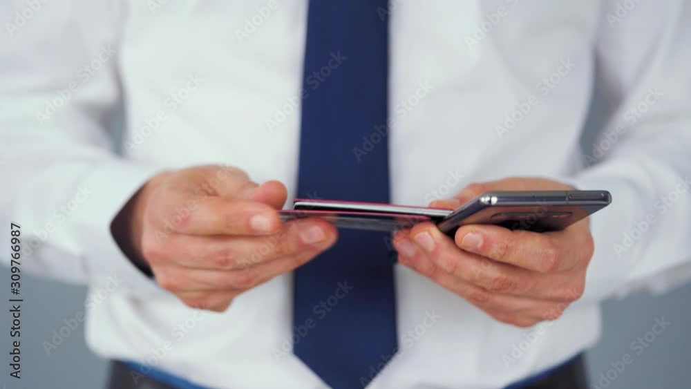 Formally dressed man selects a credit card from several and enters it number into a smartphone to pay online. Online shopping, lifestyle technology. Close-up Formally dressed man selects a credit card from several and enters it number into a smartphone to pay online. Online shopping, lifestyle technology. Close-up