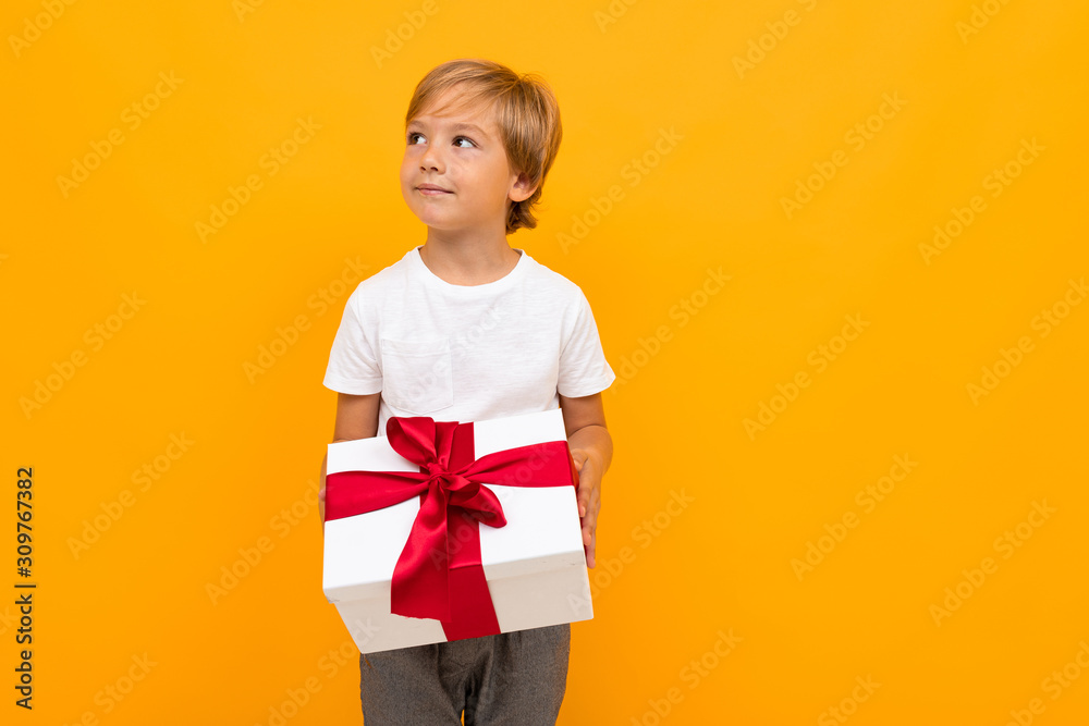 boy holds a box with a red ribbon and looks away on an orange background boy holds a box with a red ribbon and looks away on an orange background