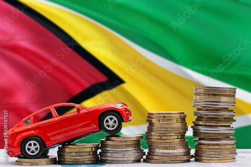 Guyana savings concept. Money for new automobile, toy car and coin piles standing on national flag background. Copy space for text.