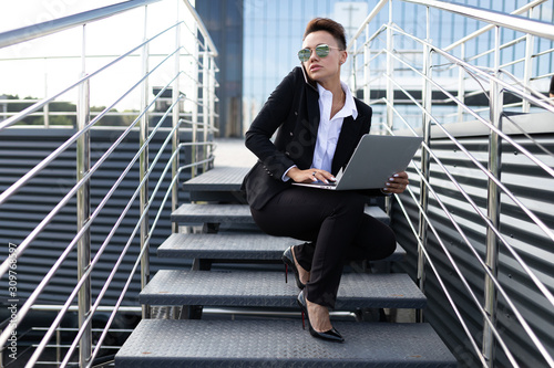 Caucasian woman in office clothes do freelance with laptop and waits colleague near the office building