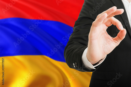 Armenia acceptance concept. Elegant businessman is showing ok sign with hand on national flag background.