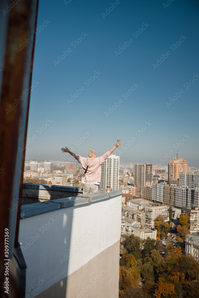 Young male holding hands up while looking at city on roof Young male holding hands up while looking at city on roof
