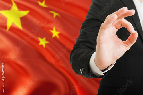 China acceptance concept. Elegant businessman is showing ok sign with hand on national flag background.