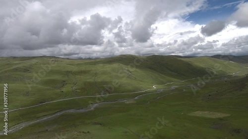 Flying over high altitude grassland, with the small river close to Tagong at around 4100 meters above sea level. Clouds are very close to the grass and it is possible to see blue sky through them.
