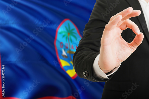 Guam acceptance concept. Elegant businessman is showing ok sign with hand on national flag background.