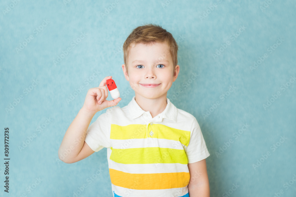 Smiling boy holding a capsule of vitamin on a blue background Smiling boy holding a capsule of vitamin on a blue background