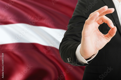 Latvia acceptance concept. Elegant businessman is showing ok sign with hand on national flag background.