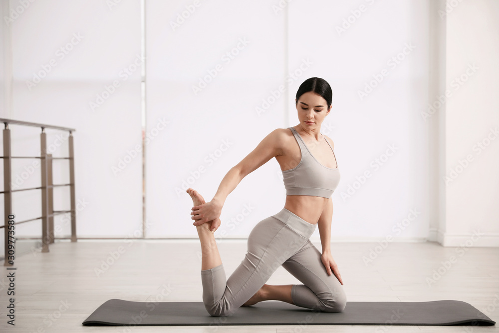 Young woman practicing One Legged King Pigeon asana in yoga studio. Eka Pada Rajakapotasana pose