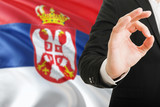 Serbia acceptance concept. Elegant businessman is showing ok sign with hand on national flag background.