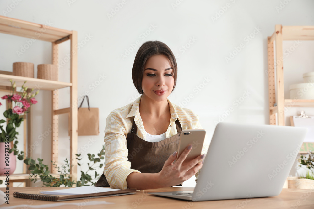 Florist with smartphone and laptop in workshop Florist with smartphone and laptop in workshop