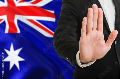 Australia rejection concept. Elegant businessman is showing stop sign with hand on national flag background.