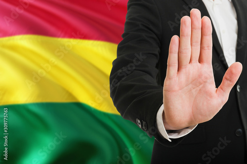 Bolivia rejection concept. Elegant businessman is showing stop sign with hand on national flag background.