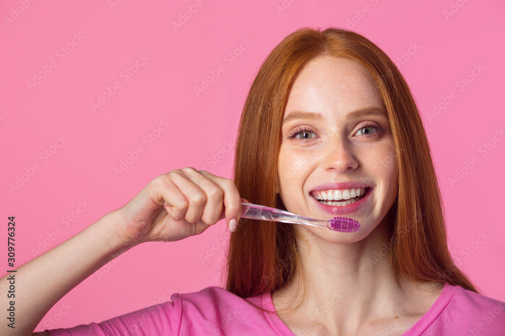 beautiful young woman with red hair on a pink background with a toothbrush beautiful young woman with red hair on a pink background with a toothbrush
