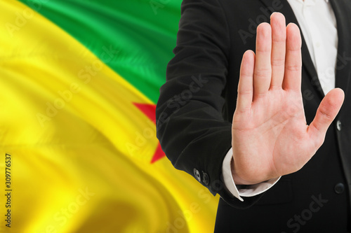 French Guiana rejection concept. Elegant businessman is showing stop sign with hand on national flag background.
