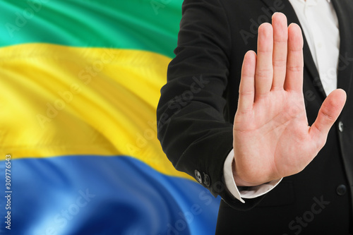 Gabon rejection concept. Elegant businessman is showing stop sign with hand on national flag background.