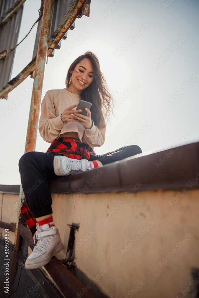 Fototapeta premium Happy young lady is typing while sitting on roof