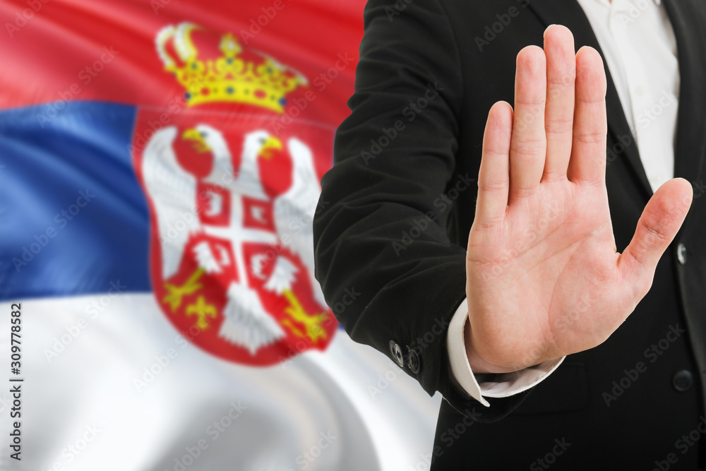 Serbia rejection concept. Elegant businessman is showing stop sign with hand on national flag background.
