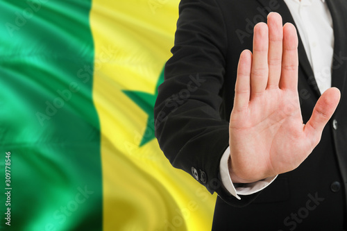 Senegal rejection concept. Elegant businessman is showing stop sign with hand on national flag background.