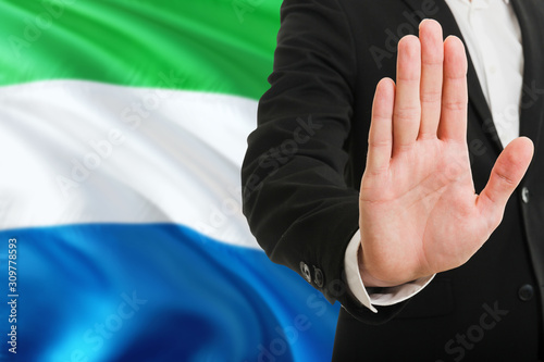 Sierra Leone rejection concept. Elegant businessman is showing stop sign with hand on national flag background.