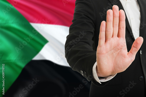 Sudan rejection concept. Elegant businessman is showing stop sign with hand on national flag background.