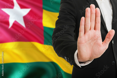 Togo rejection concept. Elegant businessman is showing stop sign with hand on national flag background.