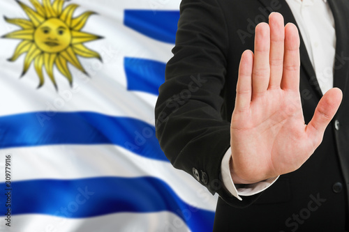 Uruguay rejection concept. Elegant businessman is showing stop sign with hand on national flag background.