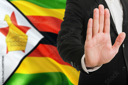 Zimbabwe rejection concept. Elegant businessman is showing stop sign with hand on national flag background.