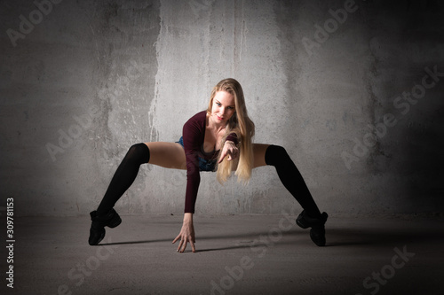 Dancer in a dance pose on a gray background. Blonde dancer with long hair in a sexy pose. Feet, dance, modern dance, hip hop, classical dance, stretching, active, fitness body