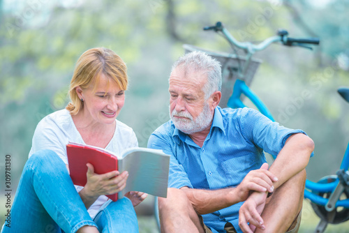 Happy elderly couple with smiling face enjoying together, reading a book in the park, spending time and relaxing time concept.
