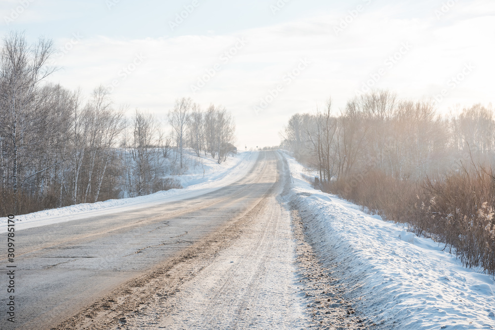 The road through the snowy forest. Asphalt road in the winter. The path through the winter forest. Winter has come. Winter landscape The road through the snowy forest. Asphalt road in the winter. The path through the winter forest. Winter has come. Winter landscape