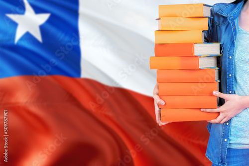 Chile national education concept. Close up of female student holding colorful books with country flag background.