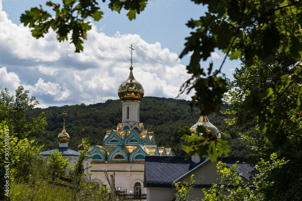 Church with a golden dome against the backdrop of mountains and clouds, in the foreground oak leaves