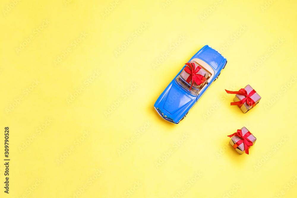 Miniature mini toy.Blue toy car with open top convertible carrying a gift with a red bow on a yellow background. View from above. Miniature mini toy Miniature mini toy.Blue toy car with open top convertible carrying a gift with a red bow on a yellow background. View from above. Miniature mini toy