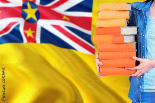 Niue national education concept. Close up of female student holding colorful books with country flag background.