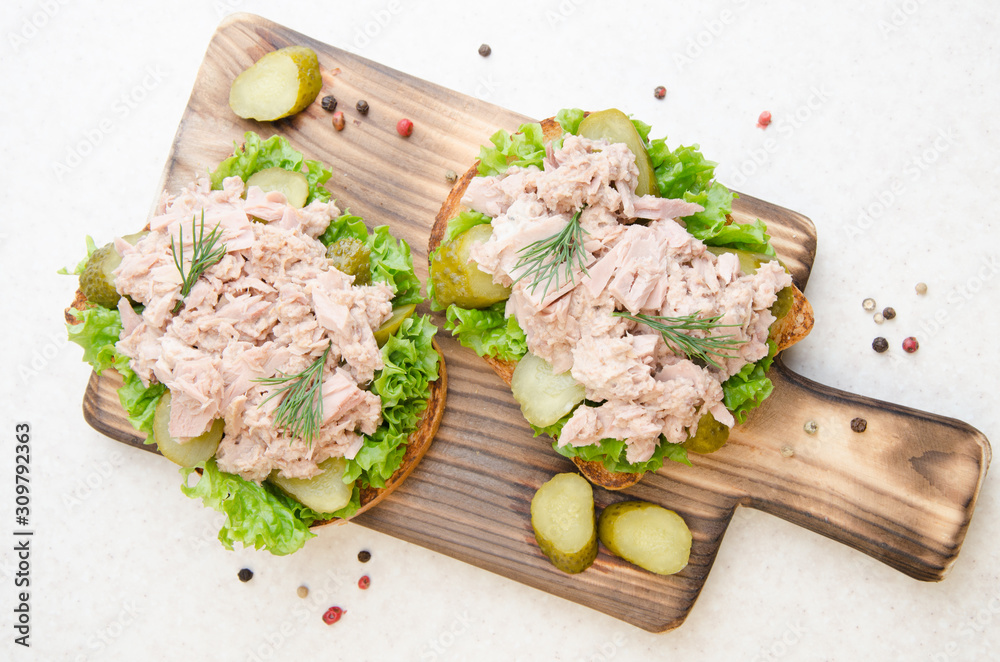 Flat lay view at homemade tuna salad sandwiches on cutting board with pickles aside