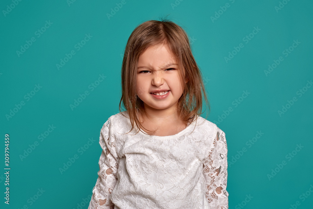 Little girl in a white sweater on a blue background. Emotions of a child. Close-up studio shot of a beautiful little girl. Little girl in a white sweater on a blue background. Emotions of a child. Close-up studio shot of a beautiful little girl.