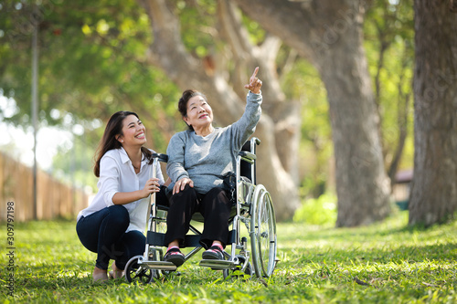 Asian senior woman sitting on the wheelchair with her daugther family happy smile face on the green park