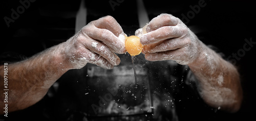 Canvastavla Baker chef breaks yellow egg into fresh dough on kitchen table, black background